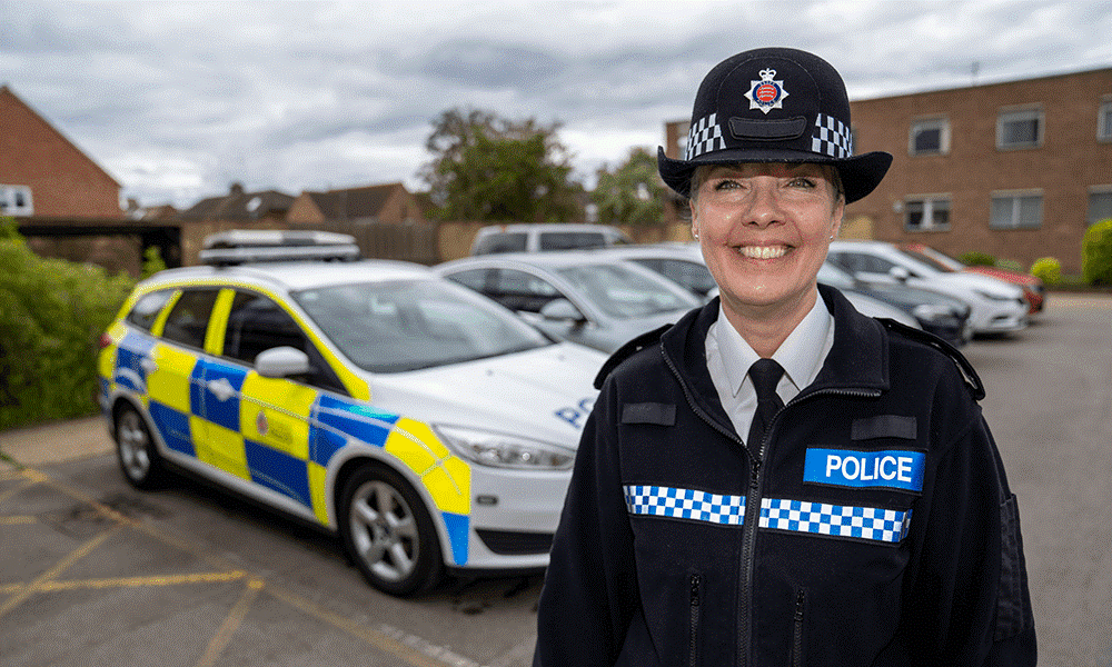 DI Tracy Betts smiling to camera in front of a police car.
