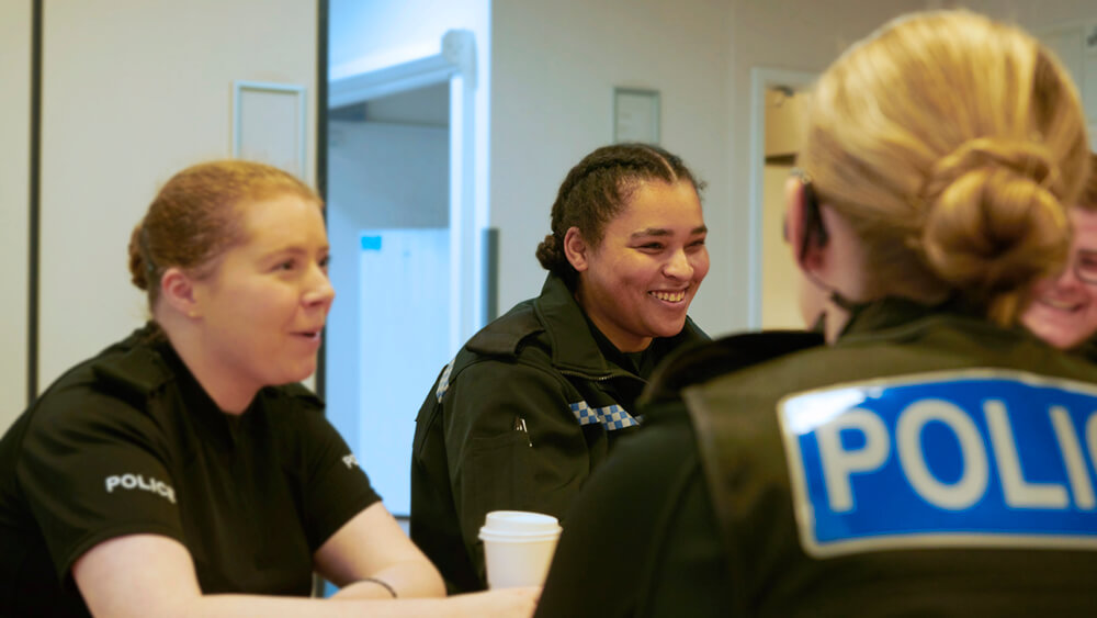 Three female officers having coffee and chatting in a meeting room.