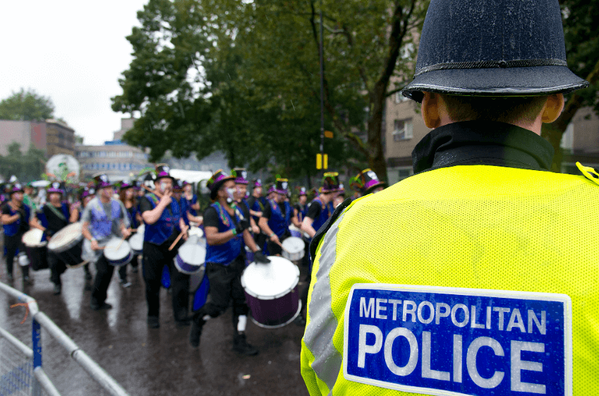 Metropolitan Police officer standing at the side of the street, watching the Notting Hill Carnival in progress. 