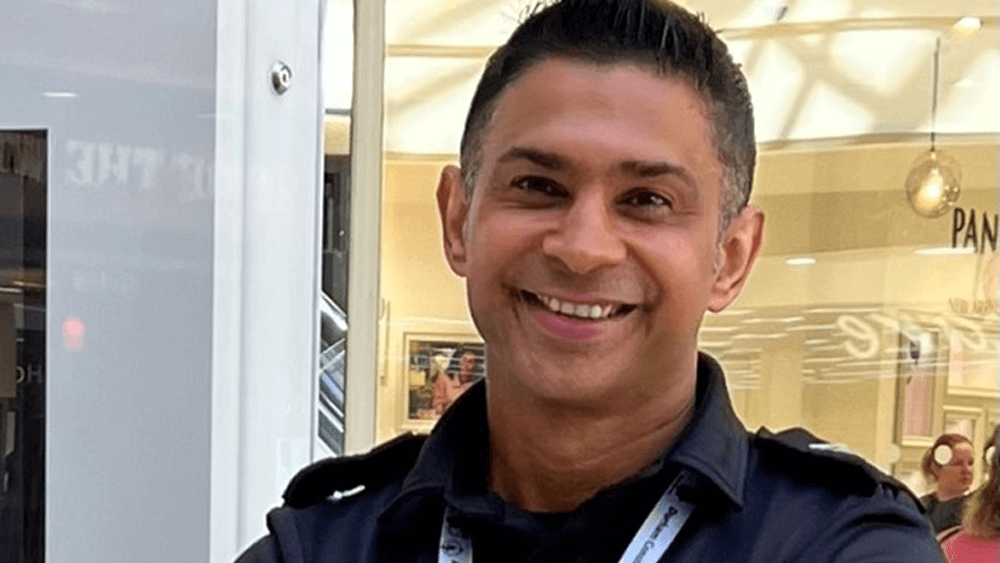 Seargeant Shaz Sadiq in uniform in a shopping centre, smiling to camera.
