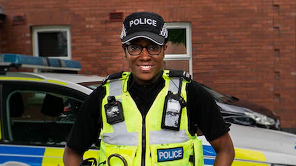 PC Alena Moulton in uniform standing outside in front of a police car. 