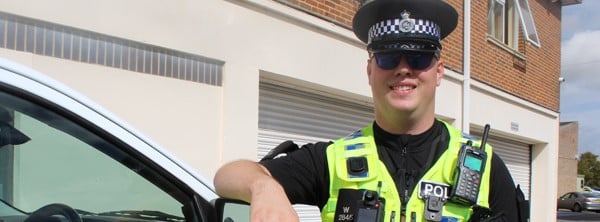 Myles standing next to police car, smiling to camera.