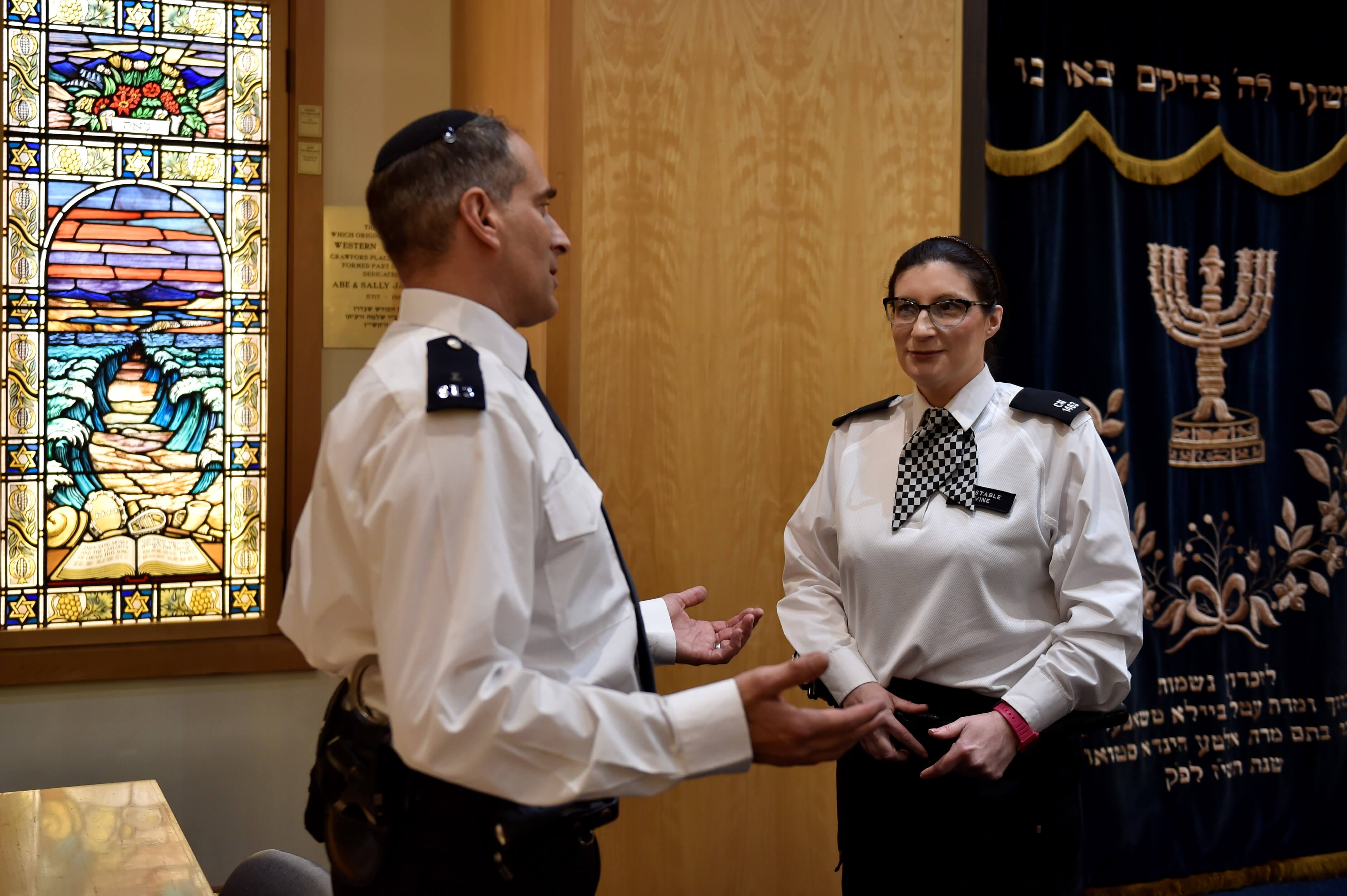 Male and female officers from the Jewish community talking in a synagogue.