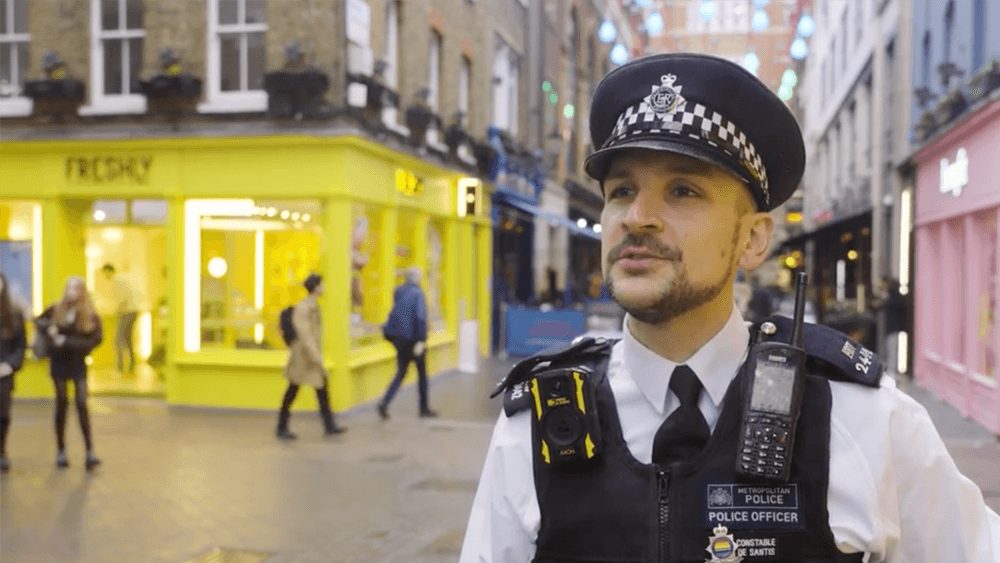 Andy De Santis in police uniform, standing in a busy shopping area.