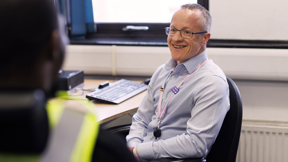 Male officer sitting at desk, smiling to camera.