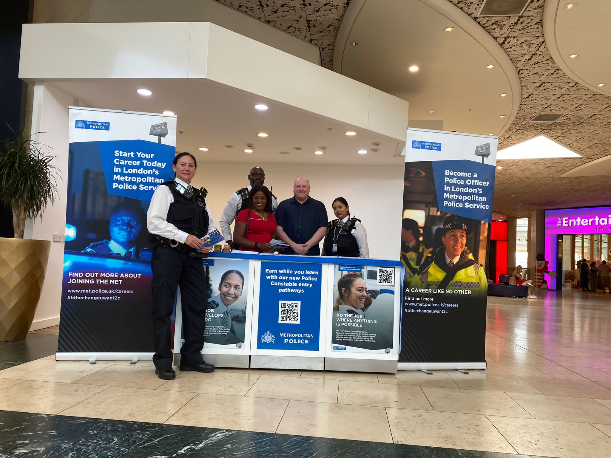 A team of four Metropolitan Police officers standing on their recruitment stand inside a shopping centre.