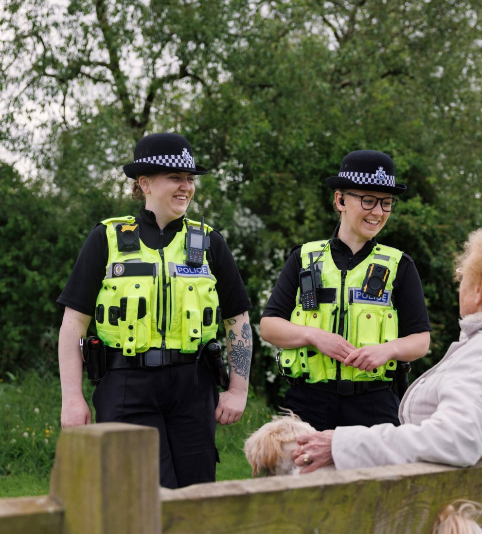 Two female officers talking to a woman sitting on a park bench.