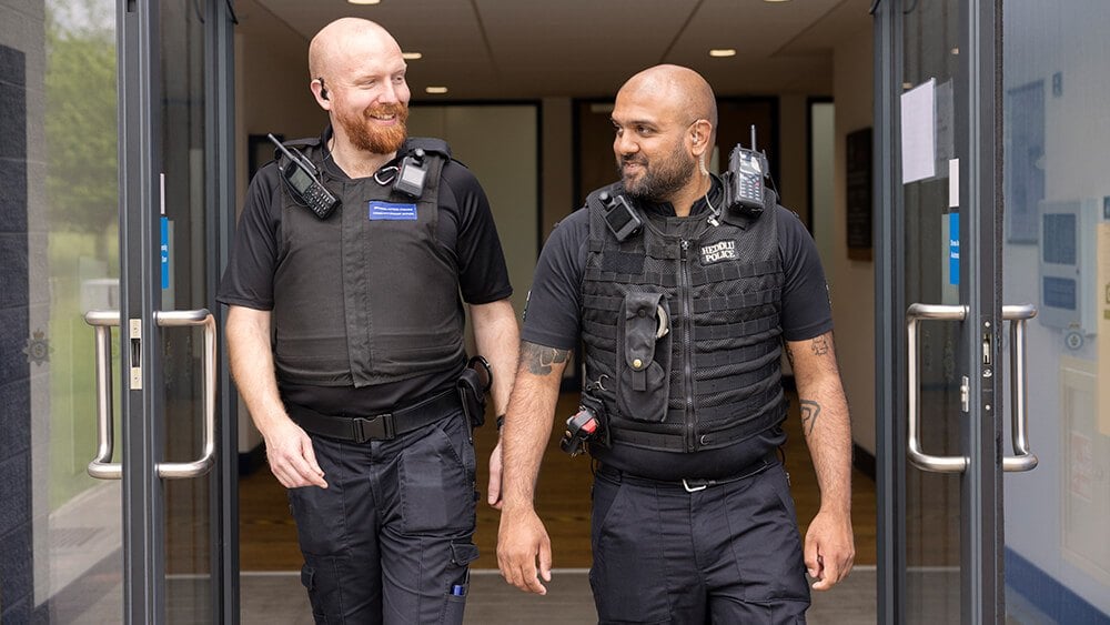Two male officers walking out of a building, smiling at each other. 