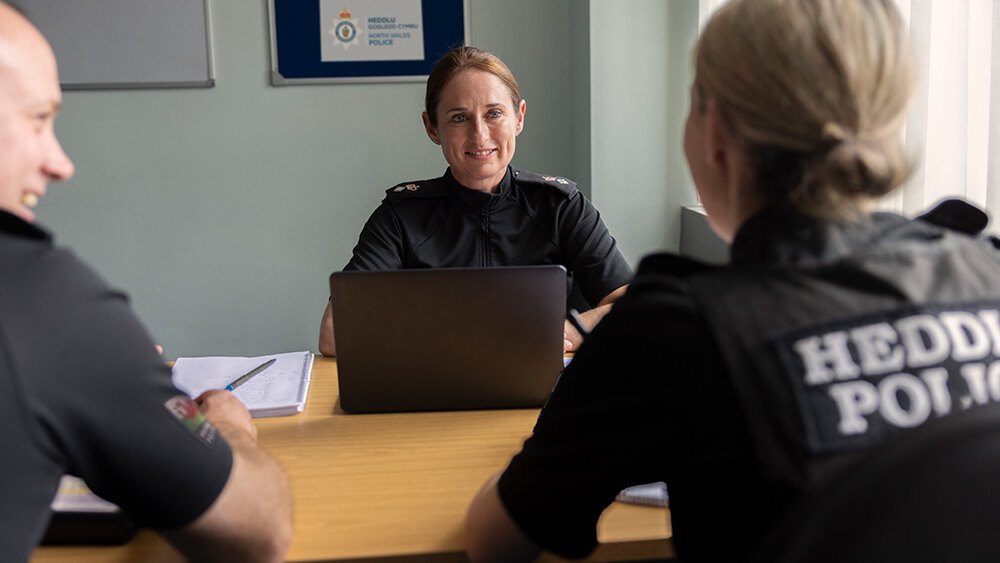 Female officer in a meeting room, sitting across a desk from a female and a male officer.